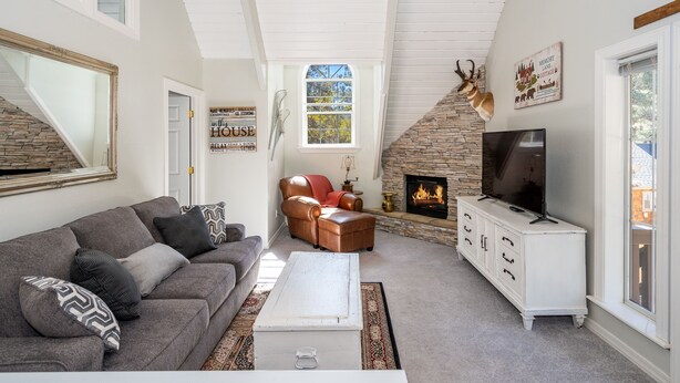A living room with a stone fireplace, a television, a leather armchair, and a large mirror. - Magdalena Cottage on 1/2 acre (Flagstaff)