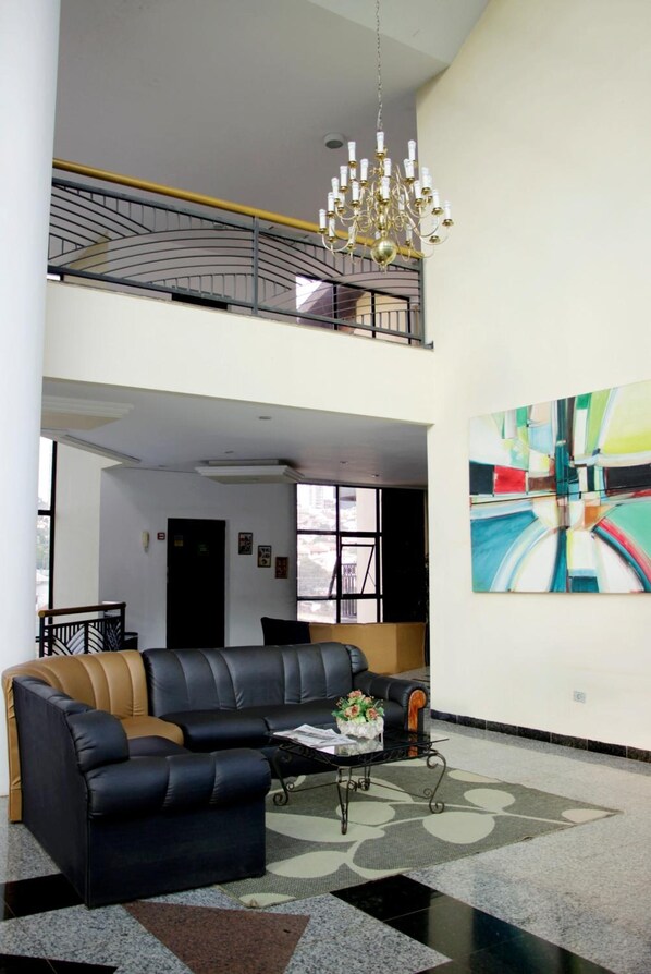 A spacious lobby with a black leather sofa, a chandelier, and a large abstract painting on the wall. - Royal Inn Hotel (Cornelio Procopio)