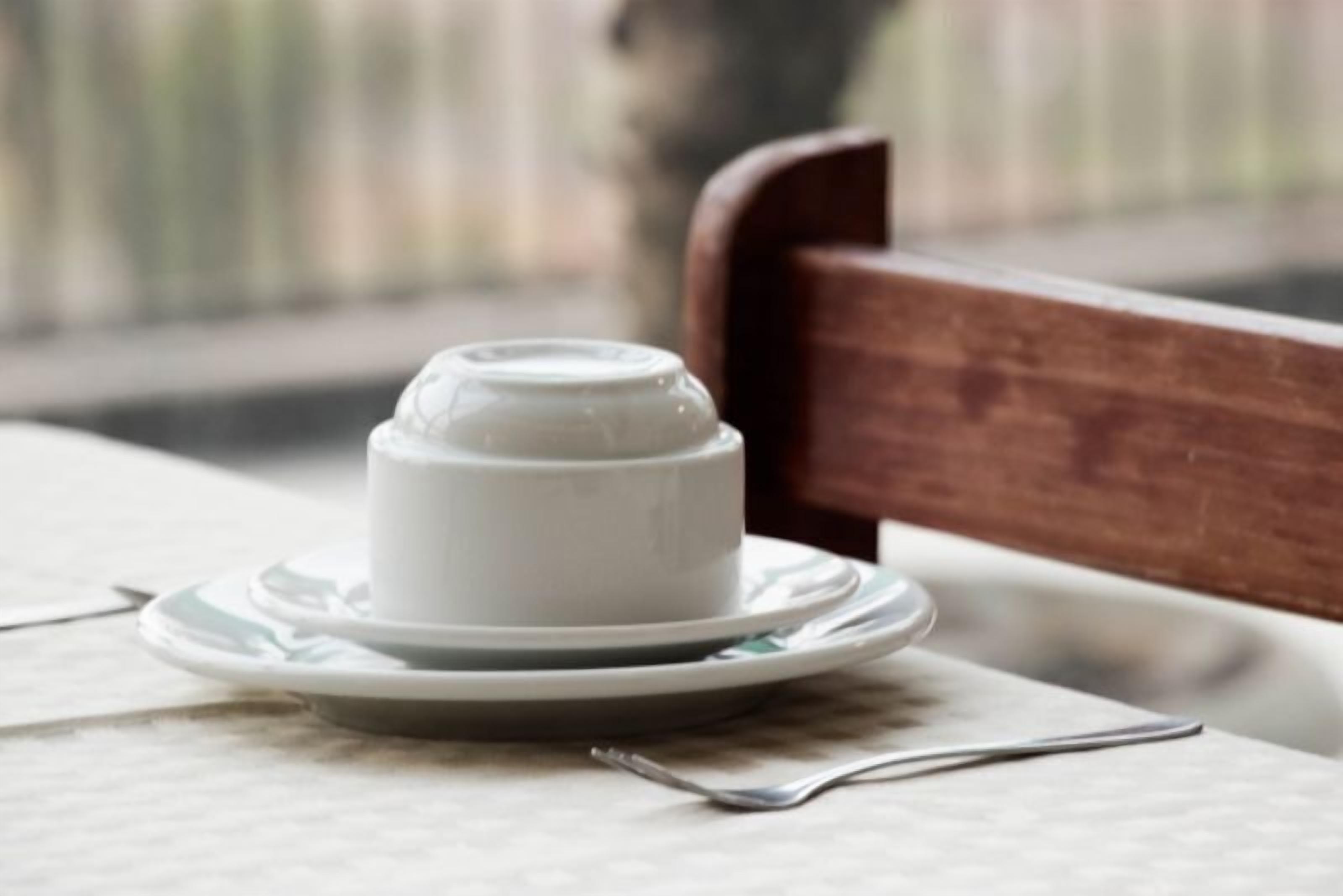 A white ceramic cup on a saucer, placed on a table with a fork beside it.