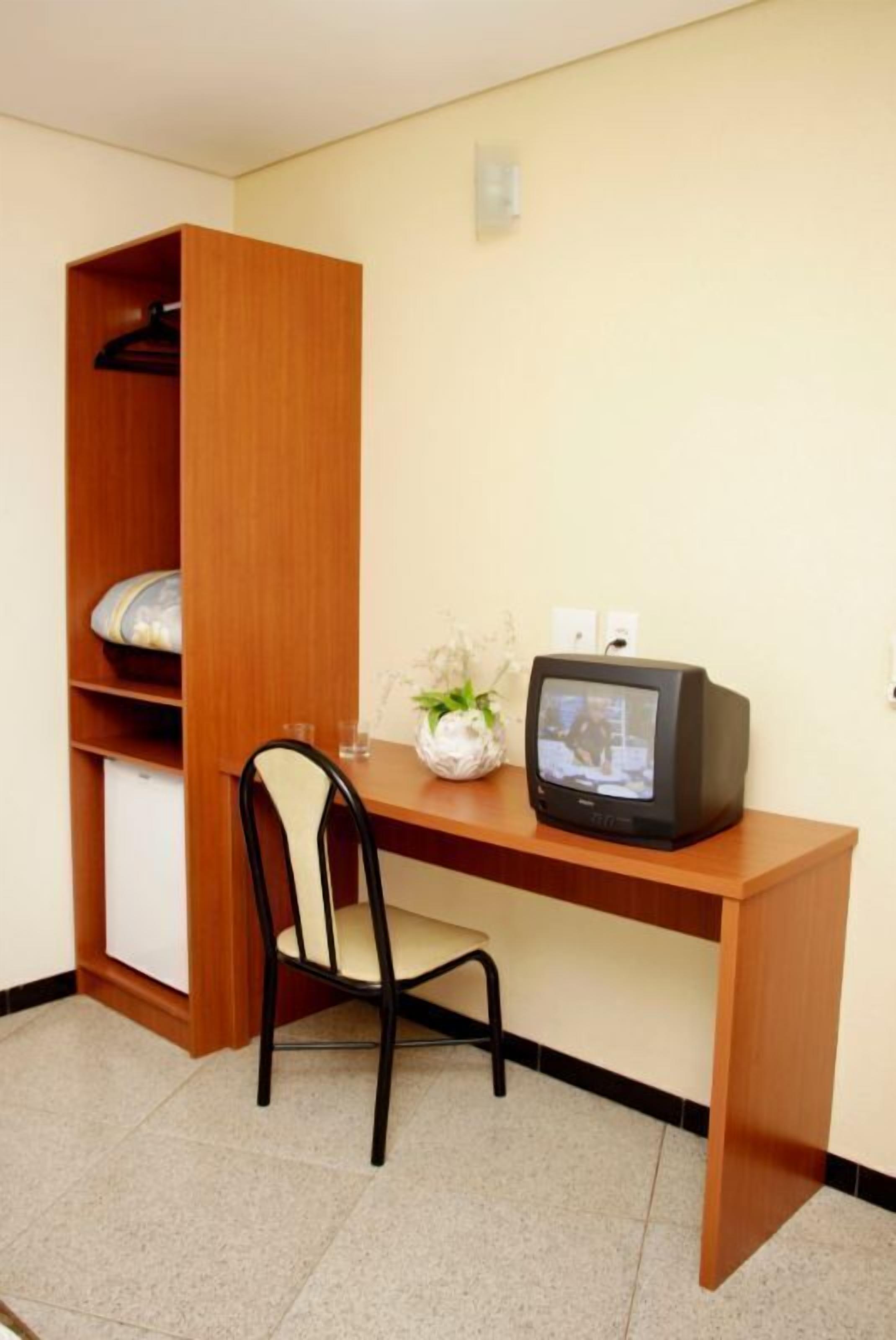 A small room with a wooden desk, a chair, a television, and a shelf with a plant.