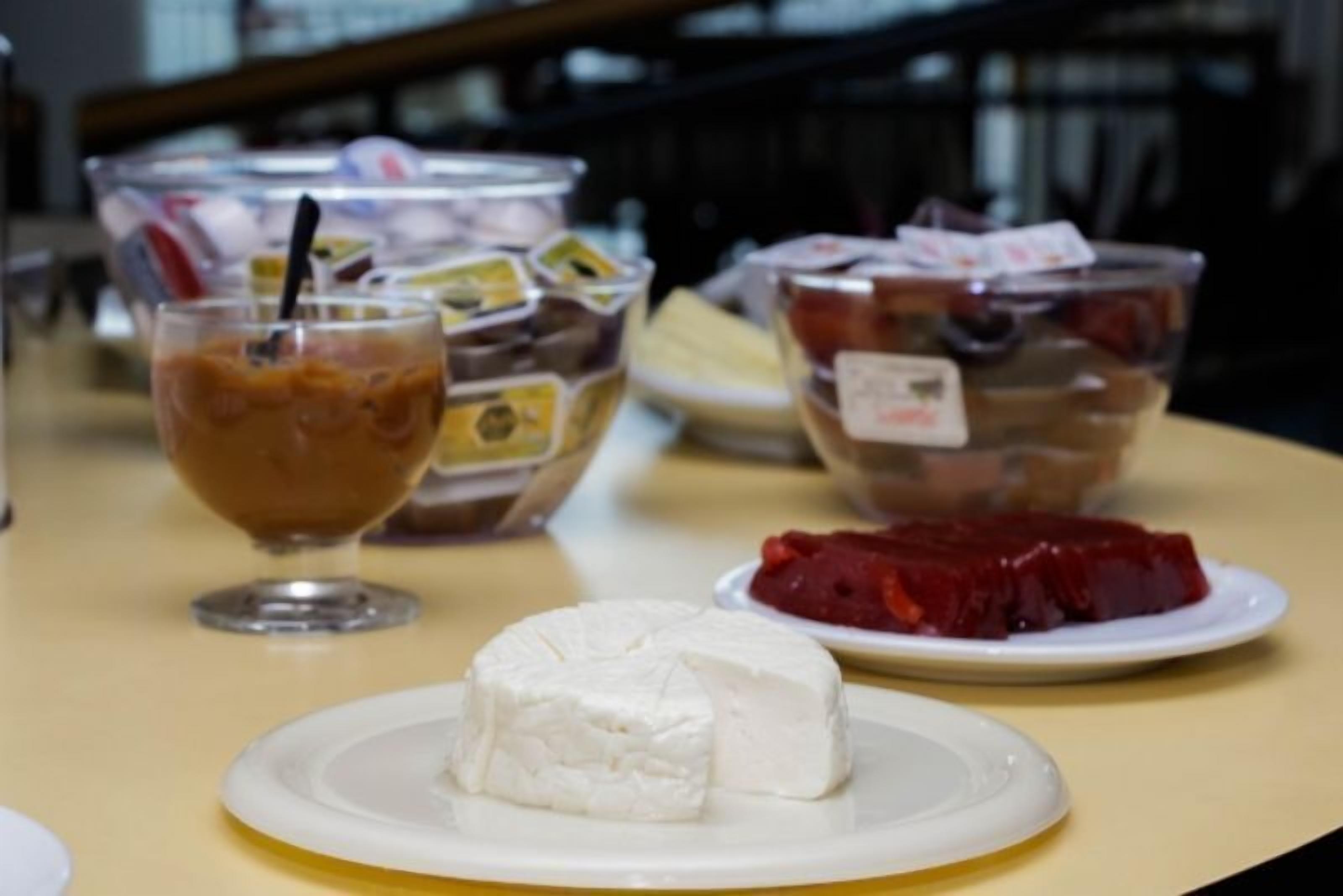 A table with a plate of white cheese, a glass of iced coffee, and two bowls of food.