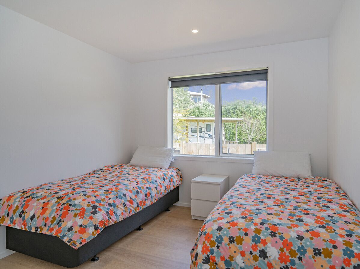 A bedroom with two beds, a small bedside table, and a window with a view of the outside.
