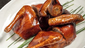 Un plato blanco con pato asado y cebollines verdes sobre una superficie de mármol oscuro.