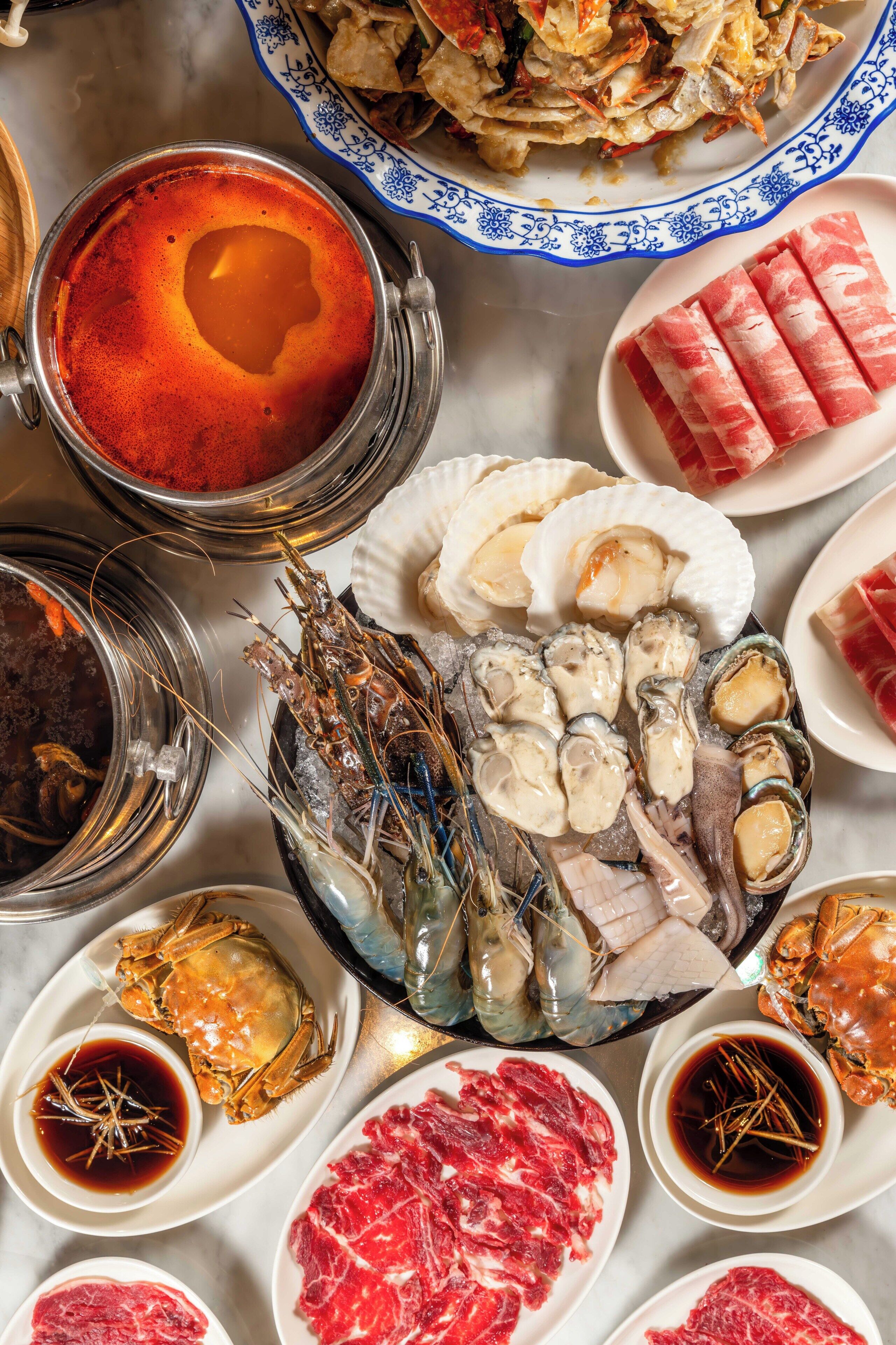 A variety of seafood dishes including lobsters, oysters, and crab legs, along with different types of meat and sauces.