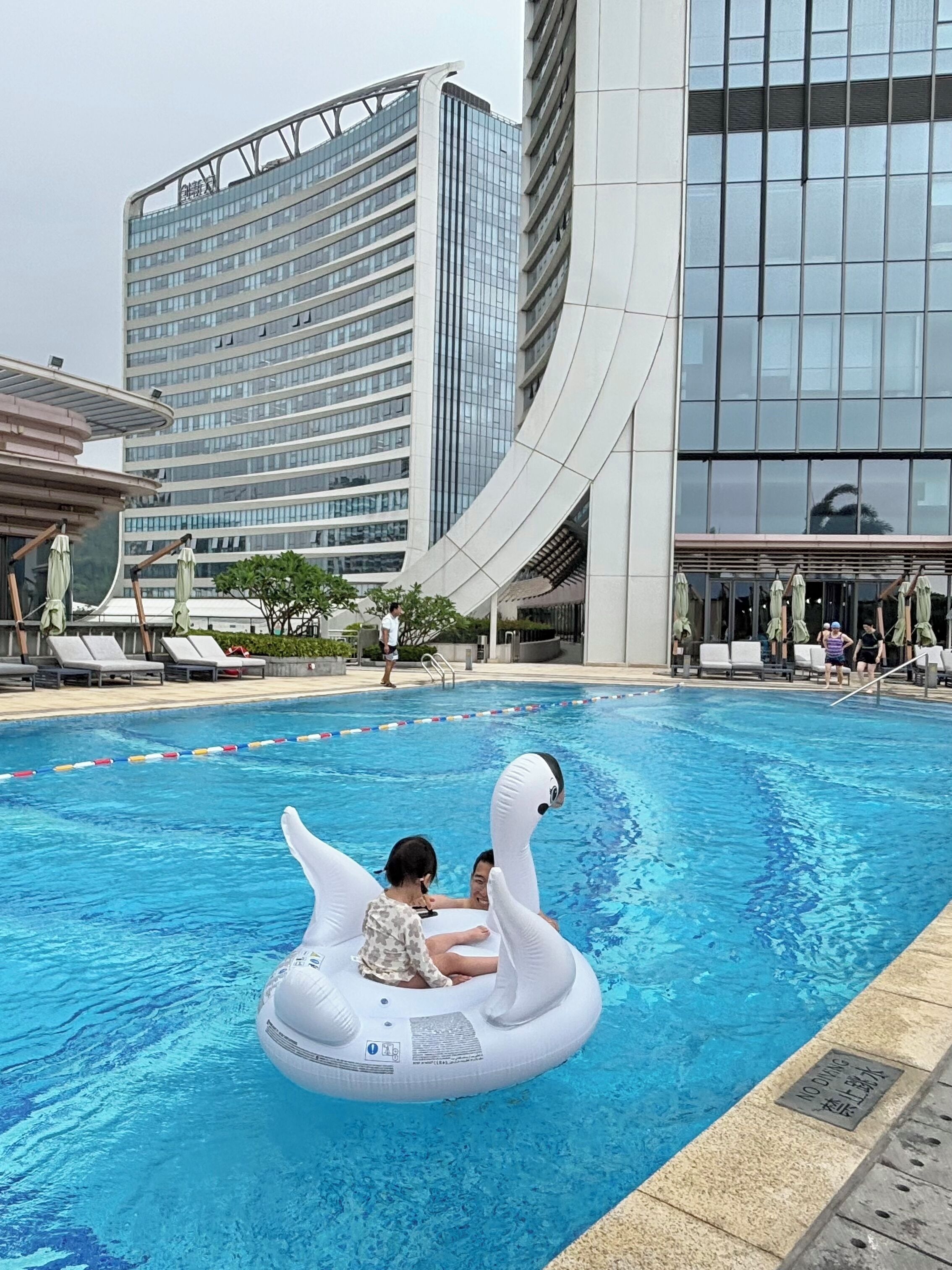 Ein Swimmingpool mit einer schwanförmigen Luftmatratze, umgeben von modernen Gebäuden.