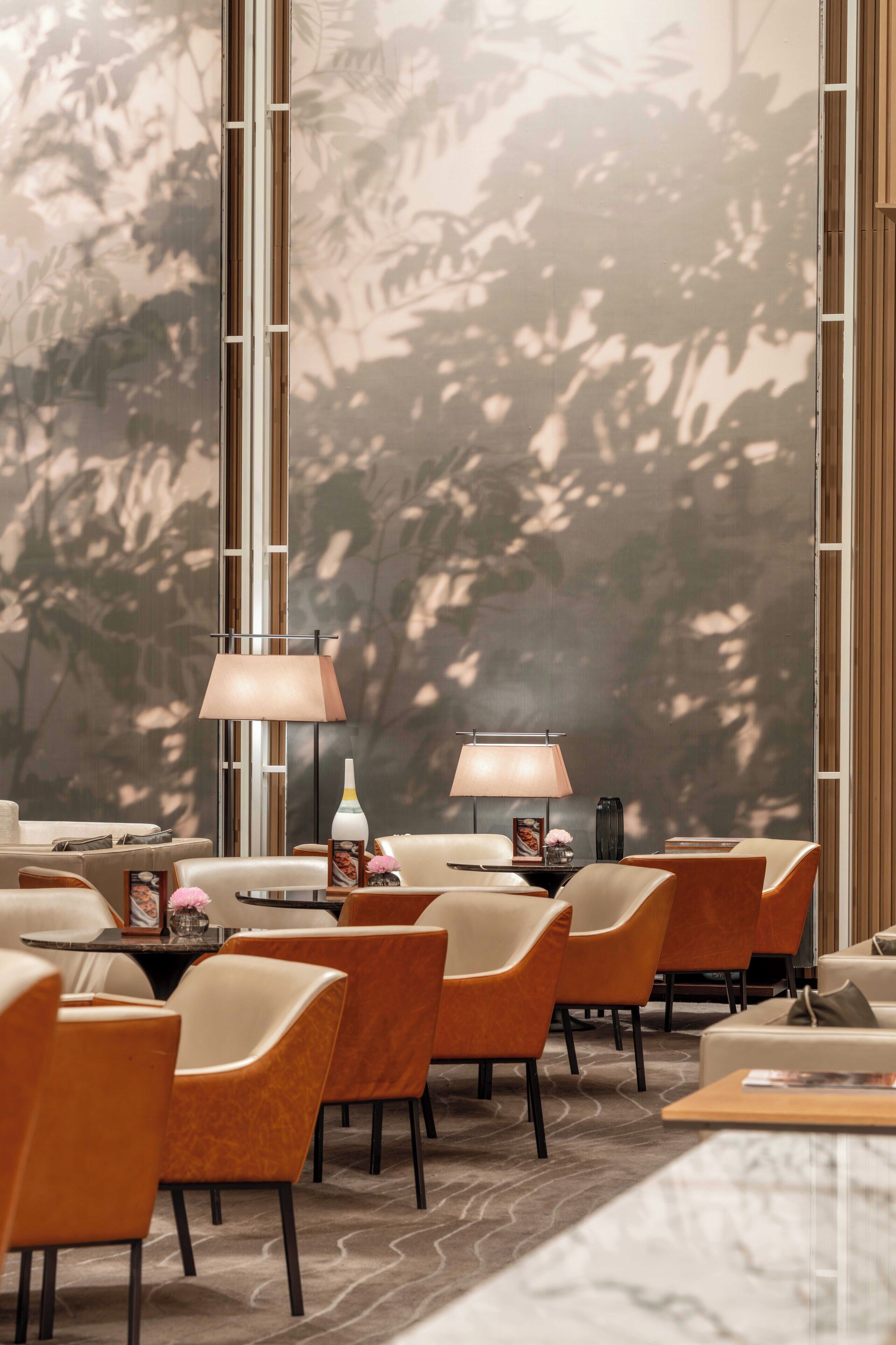 Un espace de détente moderne avec des fauteuils en cuir, une table basse en marbre et une grande fenêtre donnant sur la verdure.