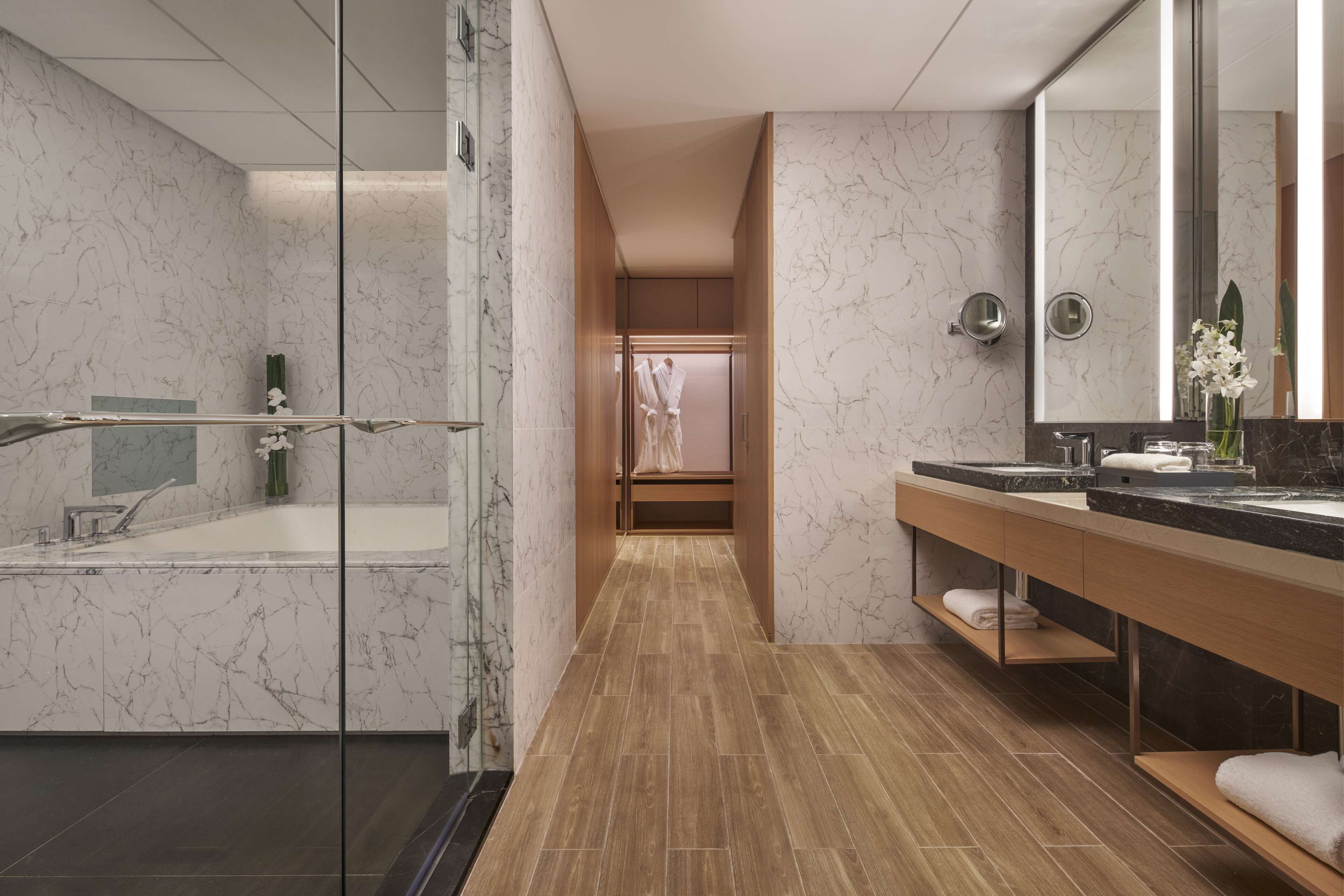 A modern bathroom with a glass-enclosed shower, a wooden vanity with a black countertop, and a marble-tiled floor.
