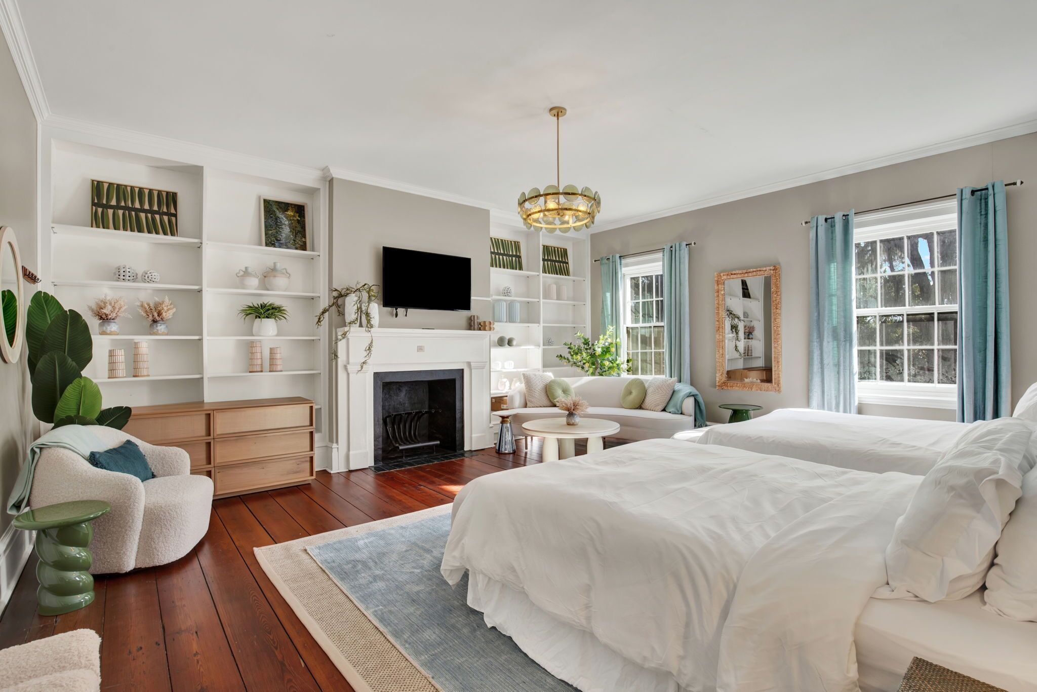 Un dormitorio amplio con una cama grande, un sofá y una chimenea. Hay estantes con objetos decorativos y un televisor.