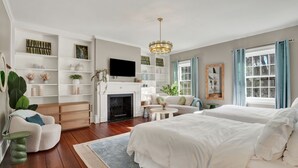 A spacious bedroom with a large bed, a sofa, and a fireplace. There are shelves with decorative items and a television.