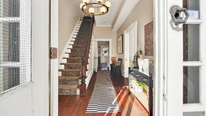A hallway with a wooden staircase, a chandelier, and a patterned rug.