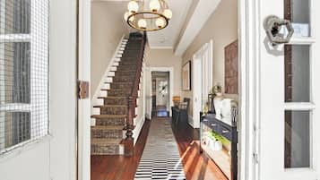 Un pasillo con escalera de madera, candelabro y alfombra estampada.
