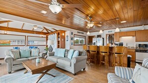 A spacious living area with a wooden ceiling, a kitchen with wooden cabinets, and a dining area with bar stools.