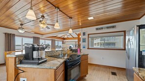 A kitchen with wooden ceiling, granite countertops, a stove, and a refrigerator.