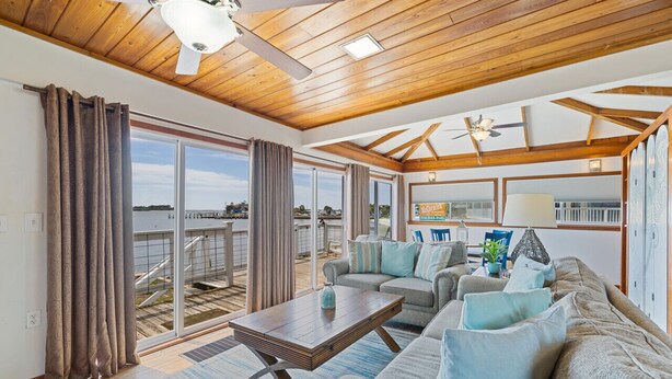 A spacious living room with a wooden ceiling, large windows, and a sliding glass door leading to a balcony.