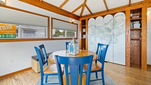 A dining area with a round wooden table, blue chairs, a decorative lantern, and a view of the outside through a window.