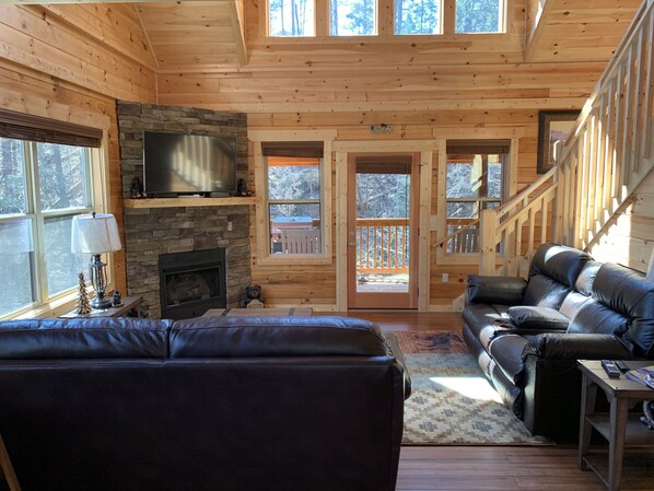 A cozy cabin interior with a stone fireplace, leather couches, and a TV mounted on the wall. - Amazing Cabin, Close to Everything/Fireplace/Jacuzzi/Hot Tub/Pool Table/Com.Pool (Pigeon Forge)