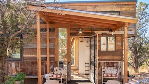 Une cabane en bois dotée d’un porche couvert, de meubles en osier et offrant une vue sur les arbres environnants.