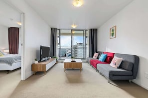 Ein modernes Wohnzimmer mit Bett, Fernseher, Sofa und einem Balkon mit Stadtblick.
