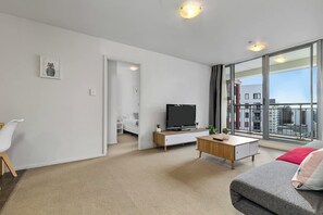 Ein modernes Wohnzimmer mit Fernseher, einer Couch, einem Couchtisch und Blick auf die Stadt durch große Fenster.