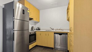 A compact kitchen with stainless steel appliances, yellow cabinets, and a dishwasher. - Wonderful Apt in CBD Neighbourhood I Zodiak Stays (Auckland)