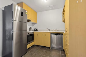 Una cocina compacta con electrodomésticos de acero inoxidable, armarios amarillos y lavavajillas.