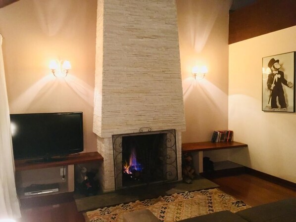 A living room with a fireplace, a flat-screen TV, and wall-mounted lights.
