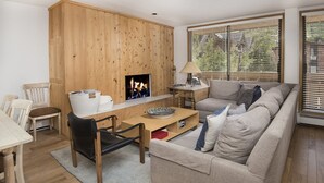 Una sala de estar acogedora con una pared de madera, chimenea, sofá, mesa de comedor y ventana con persianas.