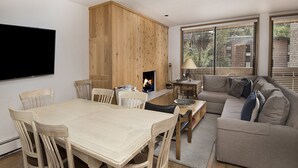 Una sala de estar moderna con una mesa de comedor de madera, un sofá gris y un televisor de pantalla plana montado en la pared.
