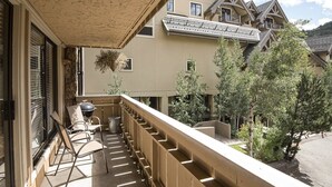 Un balcón con una parrilla, sillas y vistas a una zona residencial con árboles y edificios.