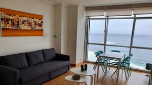A living room with a dark sofa, a small round table, and a view of the ocean through large windows.