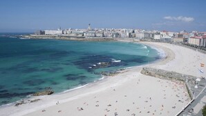 A coastal cityscape with a wide sandy beach, a promenade, and a city skyline in the background.