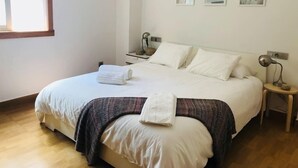 A neatly made bed with white linens and a folded towel, a bedside table with a lamp, and three framed artworks on the wall.
