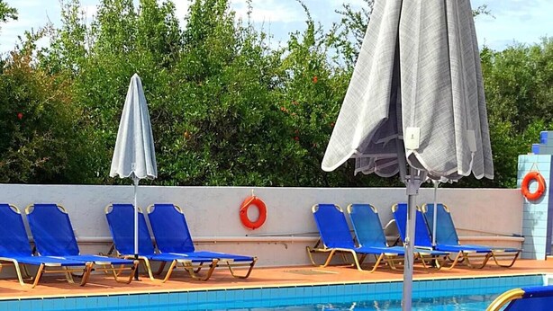 A poolside area with blue lounge chairs, a white planter with greenery, and a pool with clear blue water. - Maria Hotel (Agios Nikolaos)