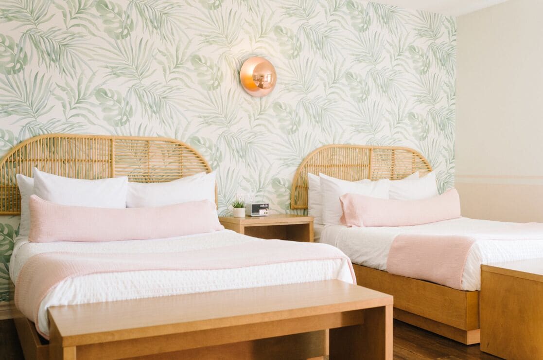 A room with two beds, each with a wooden headboard, white bedding, and a small bedside table with a radio.