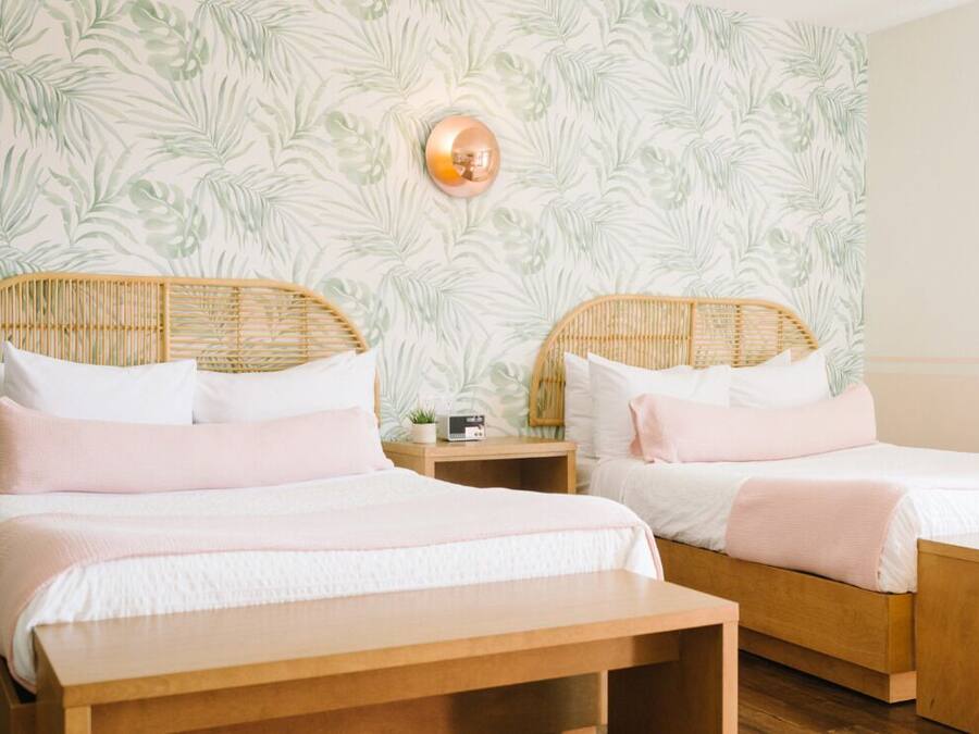 A room with two beds, each with a wooden headboard, white bedding, and a small bedside table with a radio.