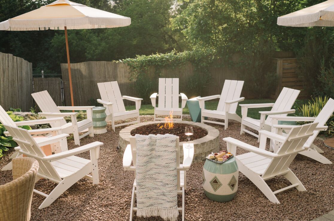 A circular seating area with white Adirondack chairs and a fire pit in the center.