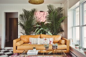 Una sala de estar acogedora con un sofá de cuero, un letrero de neón y plantas grandes.