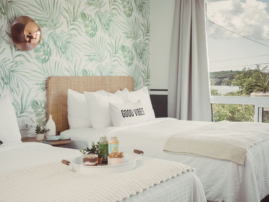 Une chambre d’hôtel avec deux lits, une grande fenêtre donnant sur l’extérieur et un mur orné d’un motif végétal.