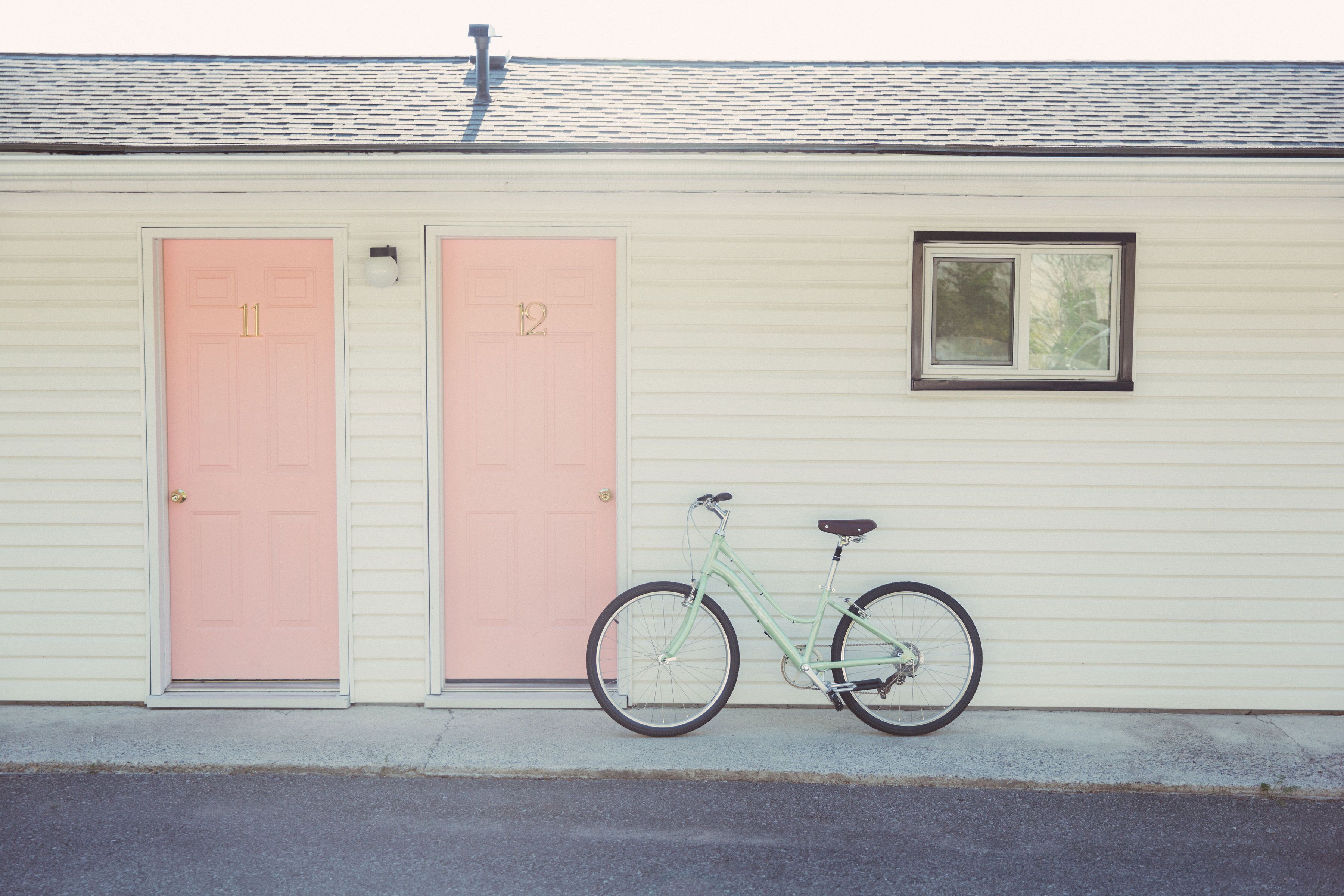 Un bâtiment avec deux portes roses, l’une portant le numéro 11 et l’autre le numéro 12, et un vélo garé devant.