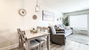 A modern living room with a grey sofa, a wooden dining table with chairs, and a hanging light fixture. - Inn Building Condo #209-Beautifully updated, view of Bear Lake (Garden City)
