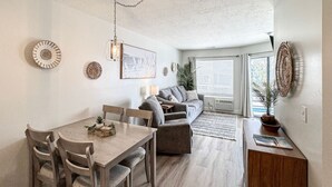 A modern living room with a sofa, a dining table with chairs, and a small kitchen area. - Inn Building Condo #209-Beautifully updated, view of Bear Lake (Garden City)