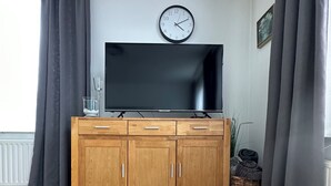 Un salon avec un meuble en bois, un téléviseur à écran plat, une horloge et des rideaux gris.