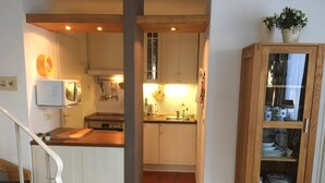 Une cuisine avec des meubles blancs, un meuble en bois doté de portes en verre et une petite plante posée sur le dessus.
