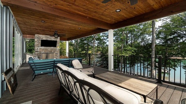 Relax on the outdoor deck with a fireplace, sofa, and chairs, surrounded by lush greenery.