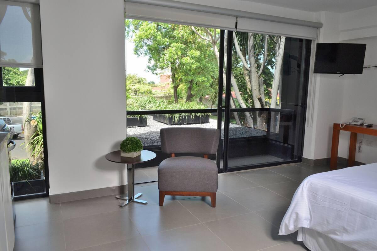 Ein Hotelzimmer mit Balkon, einem Bett, einem Sessel und einem kleinen Tisch mit Pflanze.