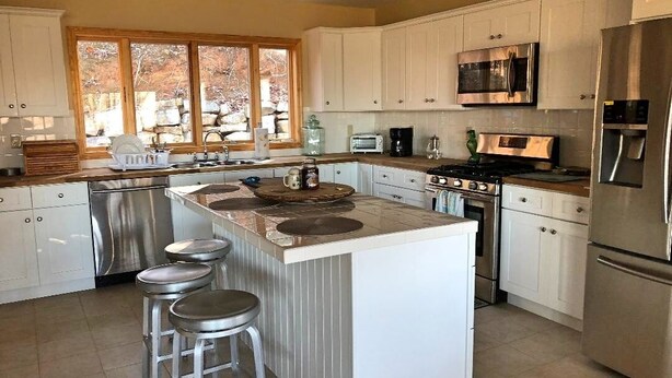A modern kitchen with white cabinets, stainless steel appliances, a large island with stools, and a window providing natural light. - Gorgeous Mountain View 8 miles from Appalachian Trail (Roan Mountain)