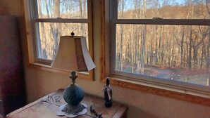 A room with a window overlooking a forest. There is a table with a lamp and a bottle on it. - Gorgeous Mountain View 8 miles from Appalachian Trail (Roan Mountain)