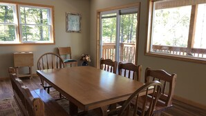 A dining area with a wooden table and benches, large windows with a view of trees, and a small table with a vase of flowers. - Gorgeous Mountain View 8 miles from Appalachian Trail (Roan Mountain)