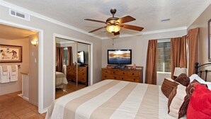 Ein Hotelzimmer mit einem großen Bett, einem Deckenventilator, einem Fernseher und Blick ins Freie durch das Fenster.