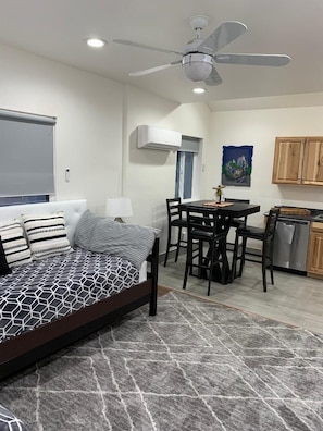 A bedroom with a bed, a ceiling fan, an air conditioning unit, a dining area with a table and chairs, and a kitchen with wooden cabinets and a dishwasher. - Beautiful 445 sq ft Studio  1 murphy bed 2 single  bed some . Ask for extras ? (Scottsdale)